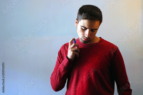 Young man using perfume or cologne on a gray background.