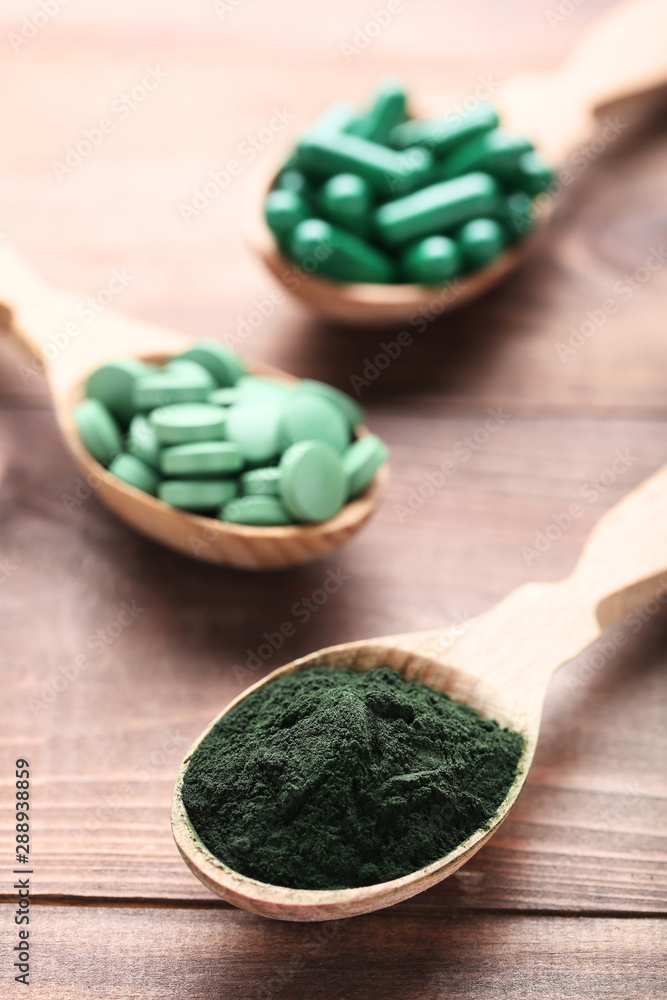 Spirulina powder and tablets in spoons on brown wooden table Spirulina powder and tablets in spoons on brown wooden table
