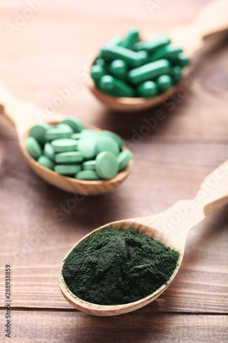 Spirulina powder and tablets in spoons on brown wooden table