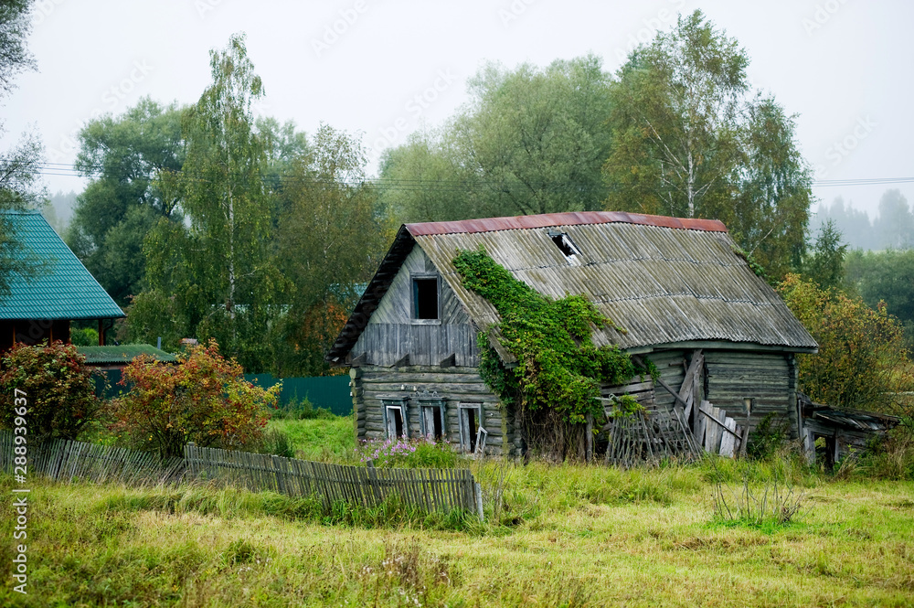 old abandoned rickety old wooden house without windows with a partially missing fence in a distant village.