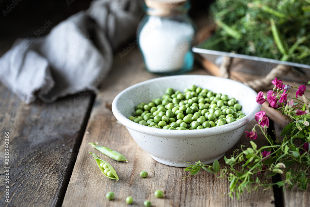 Young green peas in white bowl on wooden background. Pea flowers and daisy flowers on the table. Young green peas in white bowl on wooden background. Pea flowers and daisy flowers on the table.