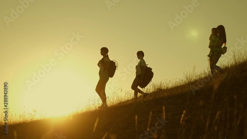 Family of tourists with children traveling at sunset. children and mom with backpacks travel down mountains in rays of the sun. Mom and daughters go camping. joint work of tourists. Slow motion