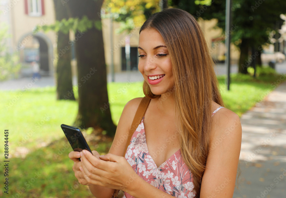 Happy beautiful fashion woman typing with phone in the street.