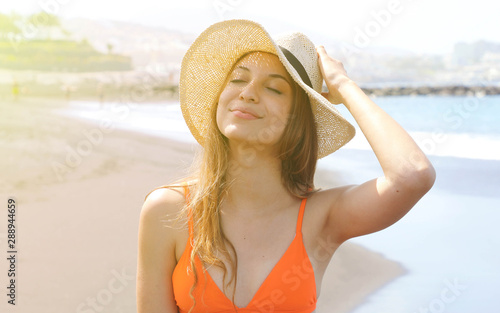 Young cheerful bikini woman with hat enjoying sun on tropical beach. Relaxing sunbathing holidays in Tenerife.