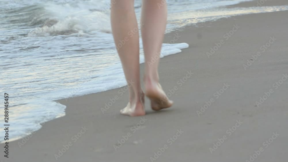 Beautiful female legs walk along the clean sand along the surf line. Sunset time Beautiful female legs walk along the clean sand along the surf line. Sunset time