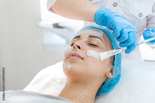 A professional cosmetologist applies a nourishing cream on the patient s face. Moisturizing  cleaning and facial skin care. Cosmetic procedures