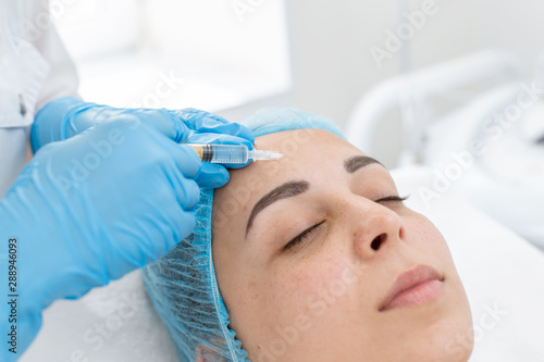 The beautician makes professional rejuvenation vitamin injections for the skin of the patient's face. A young girl is undergoing a course of spa treatments in the office of a beautician. Moisturizing