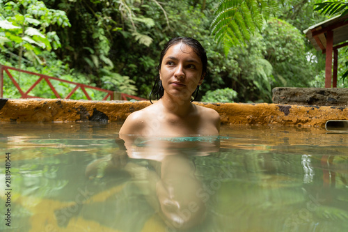 Hispanic woman relaxing in hot springs surrounded by tropical nature looking up- woman in spa © Fernanda