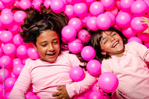 two little girls smiling and playing at pink ball pool
