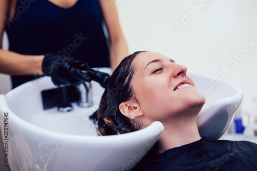 Hairdresser washing hair of a beautiful young woman in hair salon.
