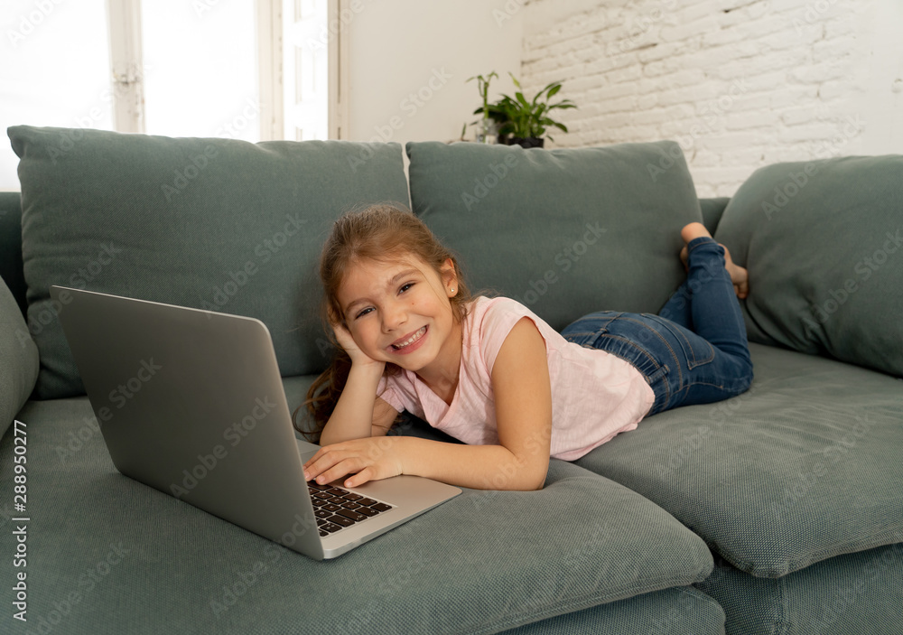 Beautiful cute charming little girl playing and surfing the internet on laptop smiling at home