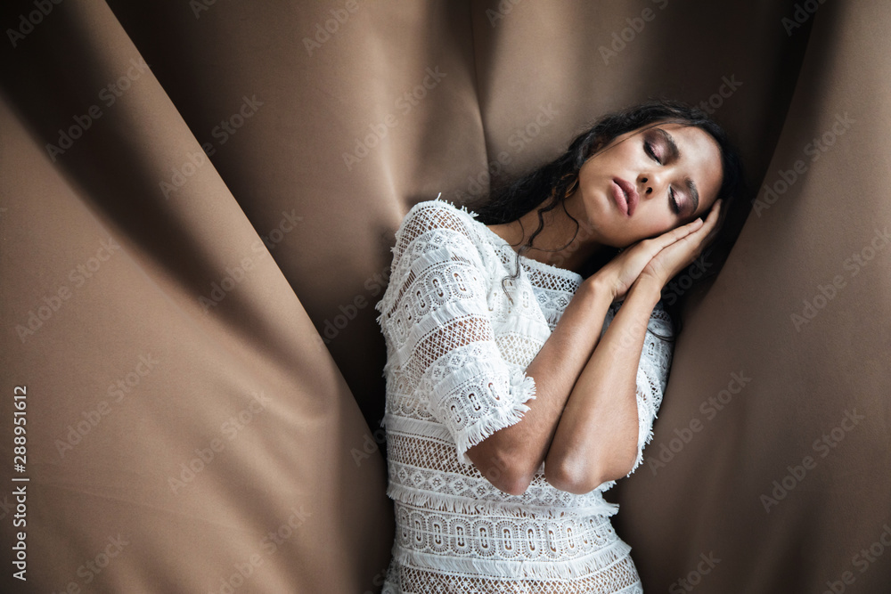 Fototapeta premium Sleeping young girl in white lacy dress on chocolate textile texture background