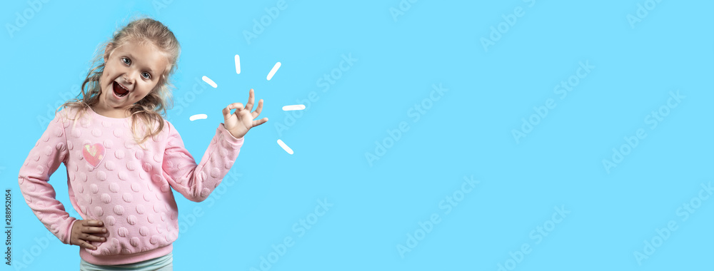 Cute cheerful girl with dimples and curly hair smiles and shows the OK sign on blue background