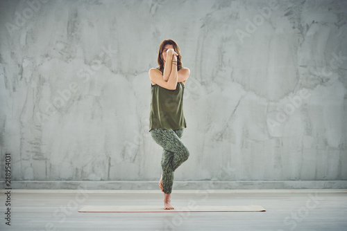 Full length of beautiful Caucasian brunette standing on the mat barefoot in Eagle yoga pose.