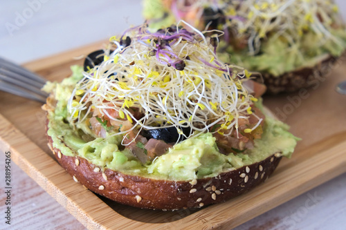 healthy brunch in a  wooden dish in table with veggie bagle with avocado, tomato, olives, outbreaks and olive oil. 