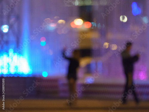 Blurred photography of the people near colorful fountain in the city park in night time. Romantic concepts of modern lifestyles.