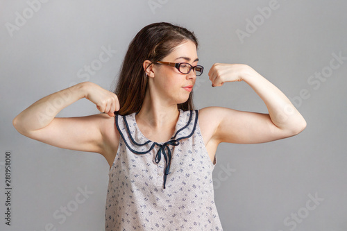 Emotions and people. A young woman in a blouse and glasses flexed her muscles, showing her strength and willingness to work
