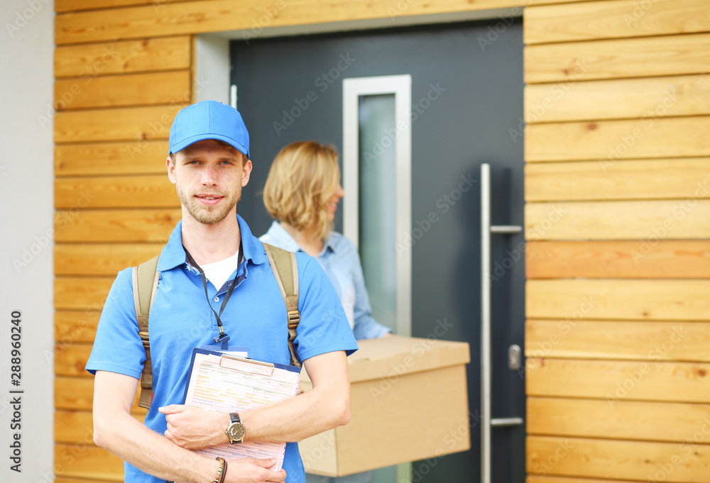 Smiling delivery man in blue uniform delivering parcel box to recipient - courier service concept. Smiling delivery man in blue uniform Smiling delivery man in blue uniform delivering parcel box to recipient - courier service concept. Smiling delivery man in blue uniform