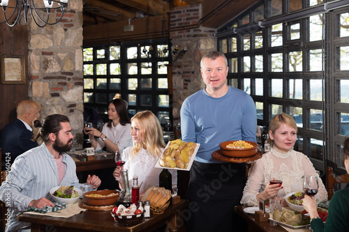 Male waiter carrying order for visitors in country restaurant