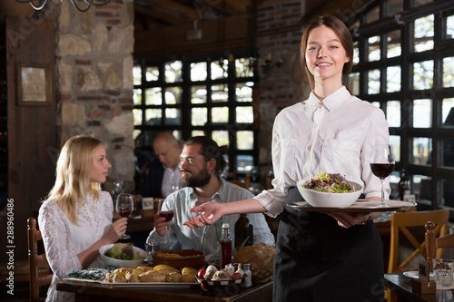 Positive woman waiter demonstrating country restaurant to visitors
