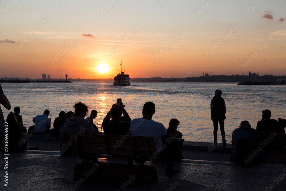 people sitting at the seaside and watching sunset and ferry.