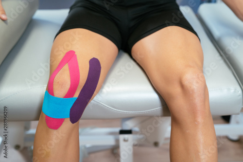 The two knees of a patient, one of them with three medical ribbons, purple, light blue and pink. Concept of muscle health and relaxation. photo