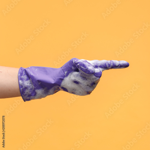 A female hand in a blue household glove with soap suds shows gestures. Yellow background.