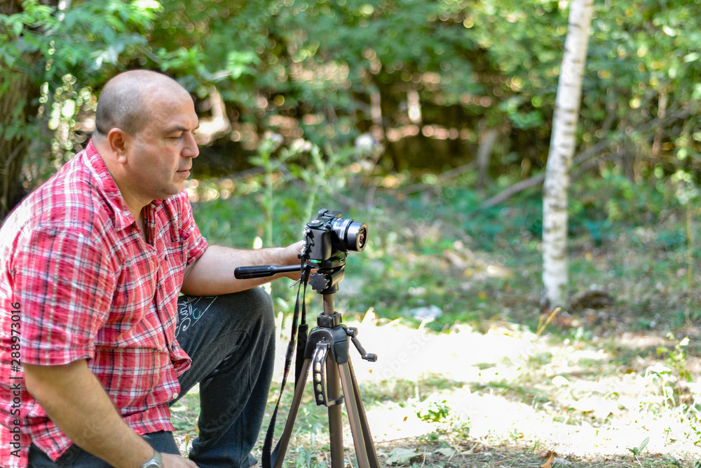 A male photographer controls a camera on a tripod in a park.