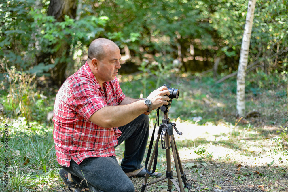 A male photographer controls a camera on a tripod in a park.