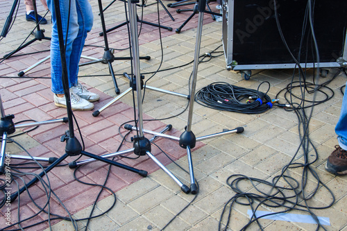 Close up view of tangled black wires and cables plugged and microphone stand on the ground, chaos after concert photo