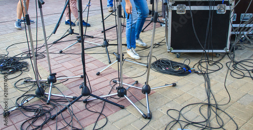 Close up view of tangled black wires and cables plugged and microphone stand on the ground, chaos after concert