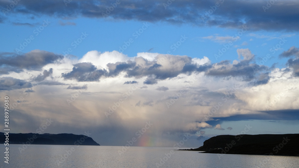 Barely visible rainbow in the middle of a fjord with scenic clouds as background in Norway