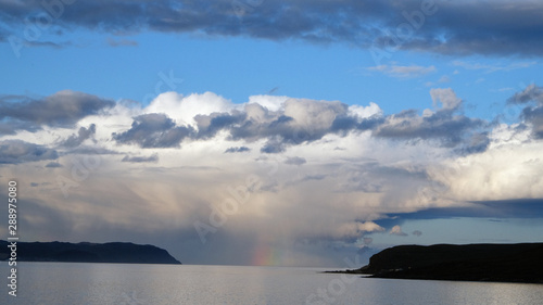 Barely visible rainbow in the middle of a fjord with scenic clouds as background in Norway