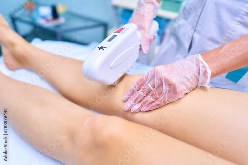 Laser hair removal of female legs in a cosmetology clinic. Doctor's hands carry out the procedure with gloves.