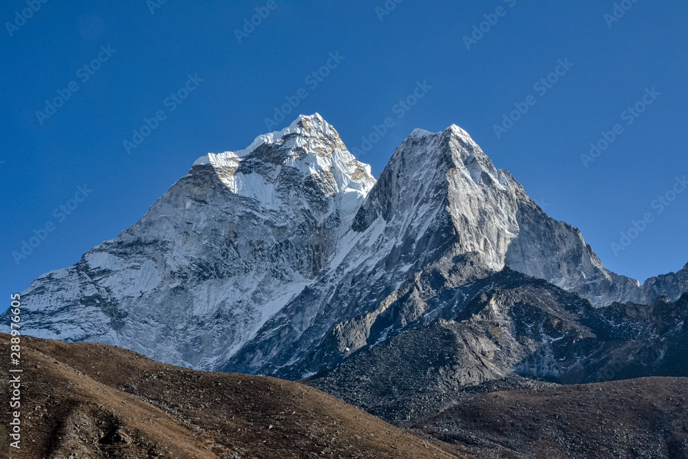 Brown and rocky hills lay in the foreground as huge snowcapped Himalayan mountains cover nearly the entire background
