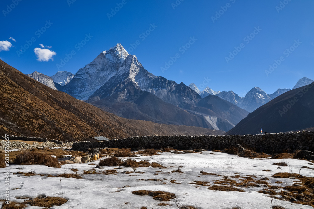 A farm field covered in ice with a stone fence plotting the available land and the Himalayan mountains in the background on a clear and sunny day