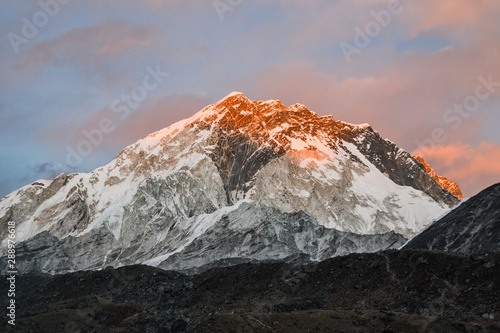 As the sun sets in Nepal, an orange glow lights up the snowcapped rocky Himalayan mountains