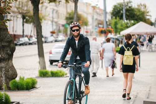 A young stylish hipster businessman going to work by bike on urban street.