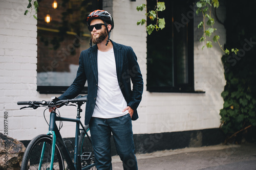 A young stylish hipster businessman going to work by bike on urban street.