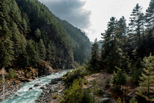 River flows through a Nepalese valley surrounded by a green pine forest on a cloudy day
