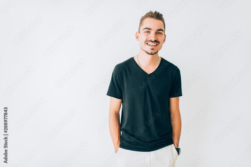 Fototapeta premium Happy young guy in black t-shirt posing on white isolated background with hands in pockets.