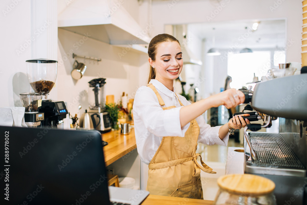 Attractive happy woman barista at the counter bar, preparing to pour coffee in a modern cafe or restaurant.