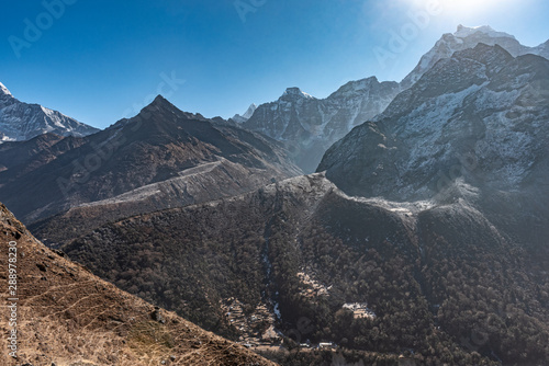 Nepalese village sits at the bottom of a valley surrounded the Himalayan mountains on a clear and sunny day