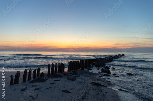 beautiful natural scene, old breakwaters in the sea at dusk against the background of an orange sunset