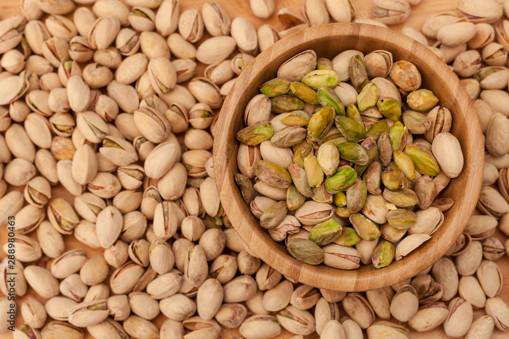 Top view of shell and peeled pistachios in wooden bowl and on wooden table Top view of shell and peeled pistachios in wooden bowl and on wooden table