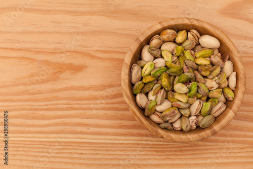 Top view of shell and peeled pistachios in wooden bowl.