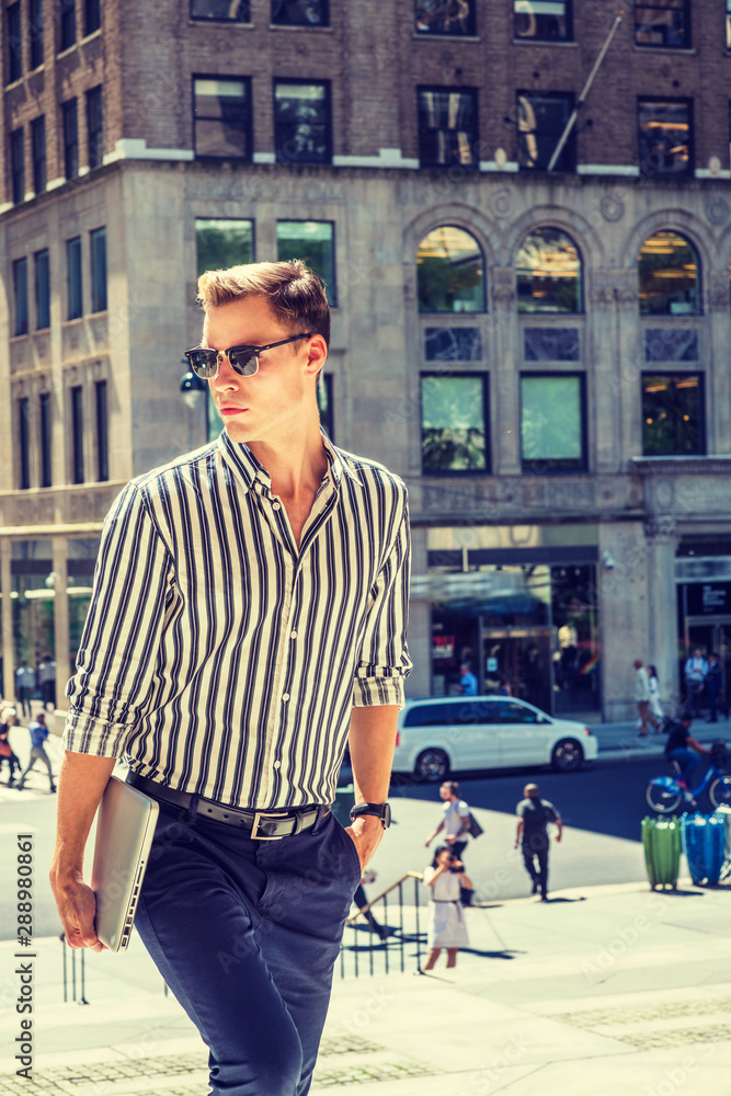 Young American man traveling, working in New York City, wearing striped, long sleeve shirt, blue pants, sunglasses, carrying laptop computer, walking up stairs from street, looking away, sad, thinking Young American man traveling, working in New York City, wearing striped, long sleeve shirt, blue pants, sunglasses, carrying laptop computer, walking up stairs from street, looking away, sad, thinking