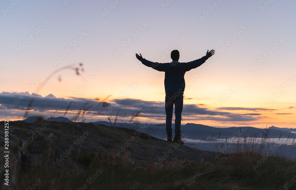 hiker celebrating success on top of a mountain above the clouds. Young man enjoying freedome, Sunrise Mountaineering sport lifestyle concept