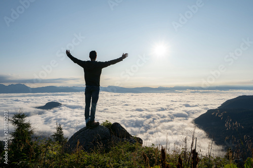 hiker celebrating success on top of a mountain above the clouds. Young man enjoying freedome, Mountaineering sport lifestyle concept © rene gamper