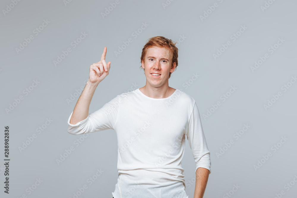 A red-haired man on a light background points. copy space A red-haired man on a light background points. copy space